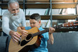 © zinkevych - Talented generation. Selective focus on a smart little boy holding a guitar and listening to his grandfather attentively while learning how to play guitar.