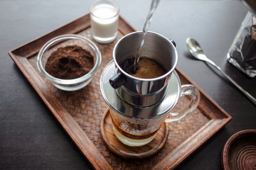 Drip, Brewing, pouring water over ground coffee contained in Vietnamese Phin Filter on dark wooden board. Selective Focus.