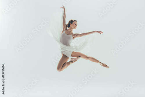 Fotomural young elegant ballerina in white dress jumping in studio, isolated on white