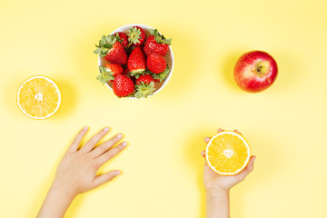 Poster - Kids hands and bowl with fresh strawberries, apple and orange on yellow background