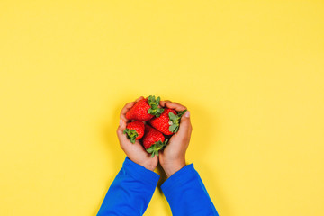 Wall Mural - Kid hands holding fresh strawberries on yellow background