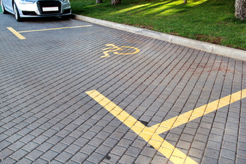 Post with disabled parking space and sign in front of parking bay in car park / Marked parking for people with special needs / Handicapped symbol, sign on asphalt, painted detail of road and street.