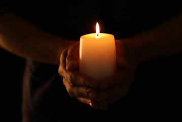 Canvas Print - Young man holding burning candle in darkness