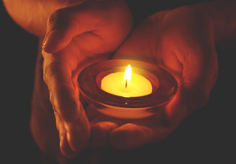 Wall Mural - Young man holding burning candle in darkness