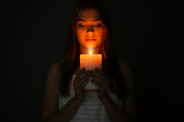 Wall Mural - Beautiful young woman with burning candle in darkness