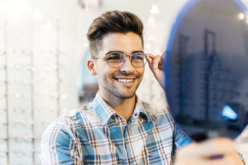 Poster - Handsome young man choosing eyeglasses frame in optical store.