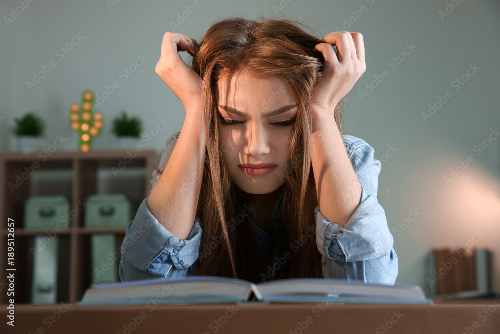 Stressed student preparing for exam at table indoors