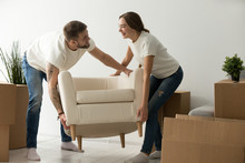 Young Couple Carrying Chair Together, House Improvement, Modern Furniture In New Home Concept, Man And Woman Moving Into Own Flat After Relocation Furnishing Living Room, Remodeling And Renovation