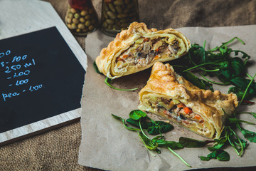 puff pastry stuffed with meat, carrots, potato pie, decorated with rucola, on a dark background Background for postcard. Menu, restaurant, recipe concept, served in. Rustik stile