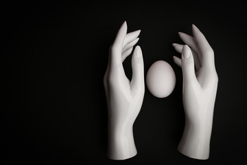 a mannequin hand on a black background about white chicken egg. 