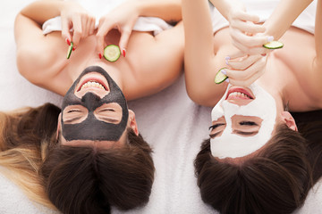 A picture of two girls friends relaxing with facial masks on over white background