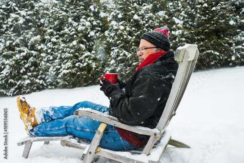Cuadros en Lienzo older man sitting in deck chair in a snow storm drinking a beverage