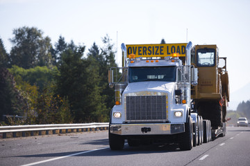 Big rig semi truck with oversize load sign and step down trailer carry and transporting digger