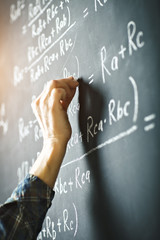 The teacher writes on a board with chalk a formula for electric current.