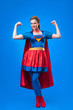 © LIGHTFIELD STUDIOS - smiling woman in superhero costume showing muscles isolated on blue