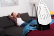 © LIGHTFIELD STUDIOS - selective focus of iron on ironing board and woman resting on sofa