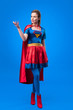 © LIGHTFIELD STUDIOS - attractive woman in superhero costume with cape gesturing isolated on blue