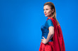 © LIGHTFIELD STUDIOS - side view of beautiful woman in superhero costume standing akimbo isolated on blue