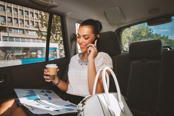 Young businesswoman talking on the phone in the back seat of the car