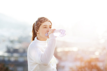 Woman drinking water during a running. Cold weather. Jogging woman in a city during a winter. Sunny day. Drinking mode. 