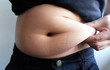 © Konkapp - woman hand catching fat body belly paunch , diabetic risk factor
