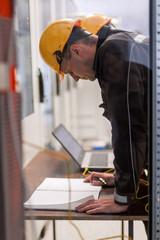 Wall Mural - two maintenance engineers inspect relay protection system with laptop comp