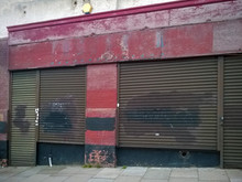 Derelict Abandoned Store With Shuttered Vandalized Shop Front With Peeling Red Paint On An Urban Street