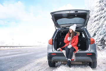 Sticker - Female tourist drinking tea near car in snowy countryside