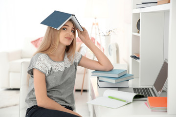 Canvas Print - Female student with book on her head indoors. Preparing for exam