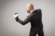 Bald man, confident manager in a white shirt, gray suit and boxing gloves makes an uppercut on a white isolated background, side view