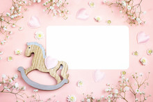Blank Paper Card With Mini Rocking Horse Toy And Gypsophila Flowers On Pink Background. Copy Space.