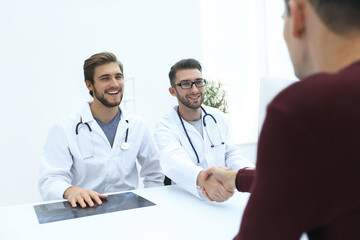 Smiling doctor at the clinic giving an handshake to his patient