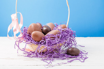 Photo of chicken , chocolate eggs, purple decorative paper in basket