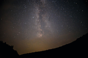 A clear night sky with a hill and trees in the foreground