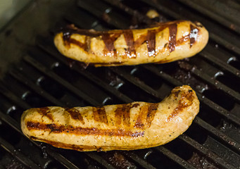 two fried meat sausages cooked in a grill with fried strips of ribs bbq shining with melted fat