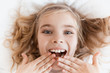 © LIGHTFIELD STUDIOS - top view of smiling adorable child lying on bed and covering mouth with hands
