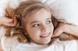 © LIGHTFIELD STUDIOS - top view of smiling adorable child lying on bed and looking away
