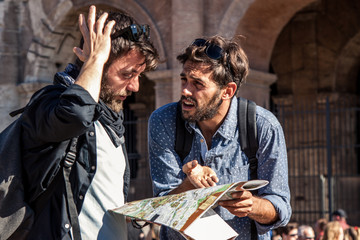 Two upset friends tourists lost in front of Colosseum in rome reading map guide for directions.