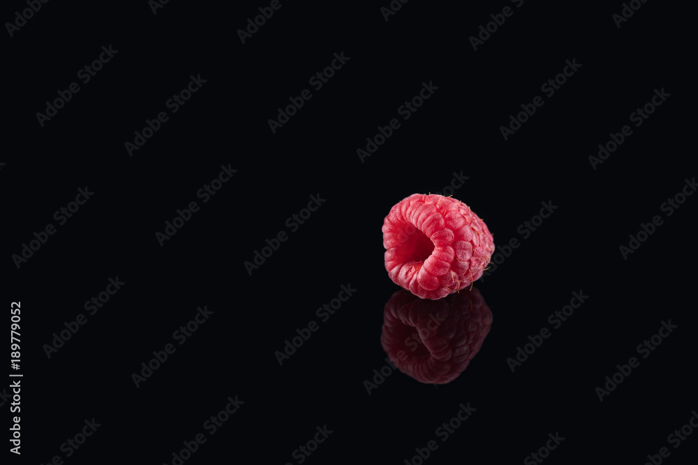 Fresh raw single raspberry on the black glass background with a ...