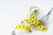 The measuring tape is yellow, wrapped around a fork lying on a white surface.