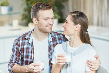 Poster - Yougn man and woman with glasses of milk looking at one another and talking by breakfast