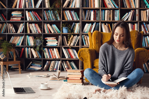 Fotografie, Obraz Young woman writer in library at home creative occupation sitting writing notes
