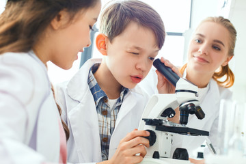 Little kids with teacher in school laboratory looking in microscope close-up