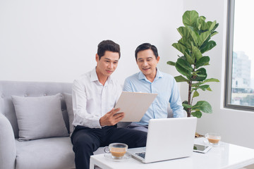 Two confident young businesspeople using a laptop discuss information while sitting on a sofa in a modern office