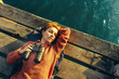© tinyakov - Beautiful Young Girl Lies On Pier, Holds Binoculars In Hand And Dreams, Top View