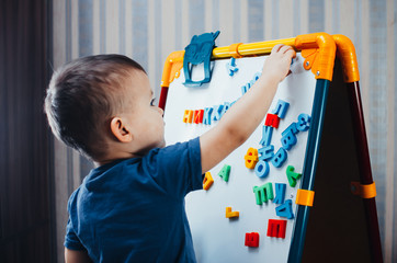 the little boy is studying the letters, using the easel with a magnetic surface