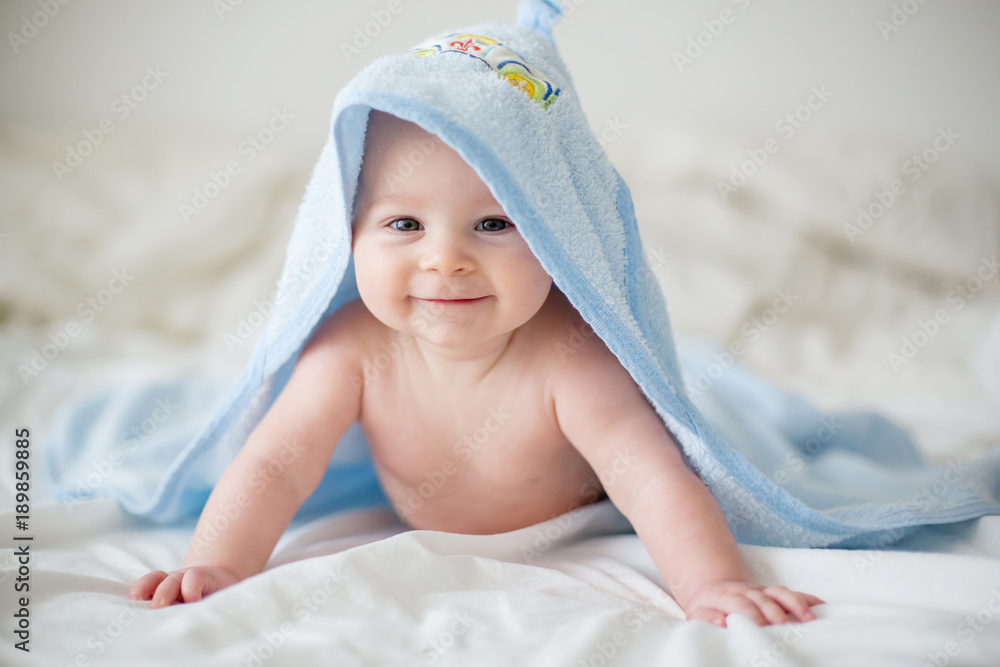 Cute little baby boy, relaxing in bed after bath, smiling happily - obrazy, fototapety, plakaty 