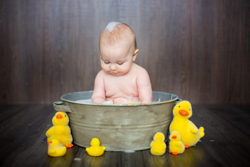 Sticker - Cute baby playing with rubber duck while sitting in metal basin