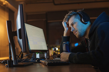 Side view calm programmer looking at screen of gadget while listening music. He tasting can of energy liquid. Job concept