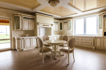 Luxury modern fitted kitchen interior. Kitchen in luxury home with beige cabinetry. Table and chairs